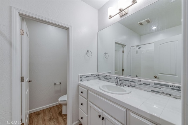 bathroom with tasteful backsplash, a shower, hardwood / wood-style floors, vanity, and toilet