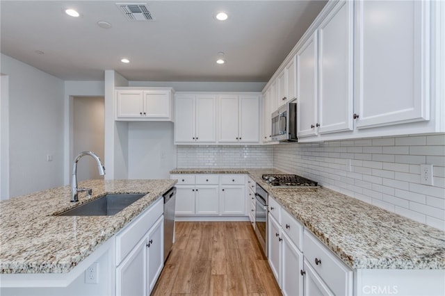 kitchen with light hardwood / wood-style floors, white cabinets, stainless steel appliances, a center island with sink, and sink