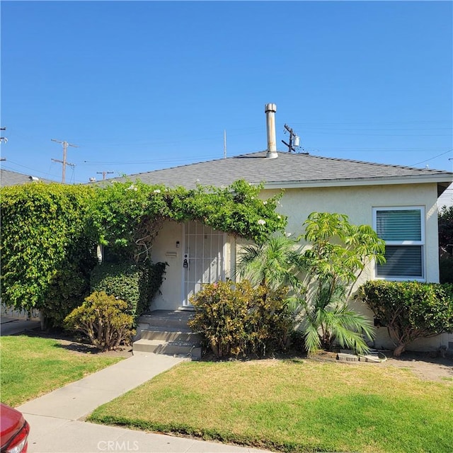 view of front of home featuring stucco siding, a shingled roof, and a front yard