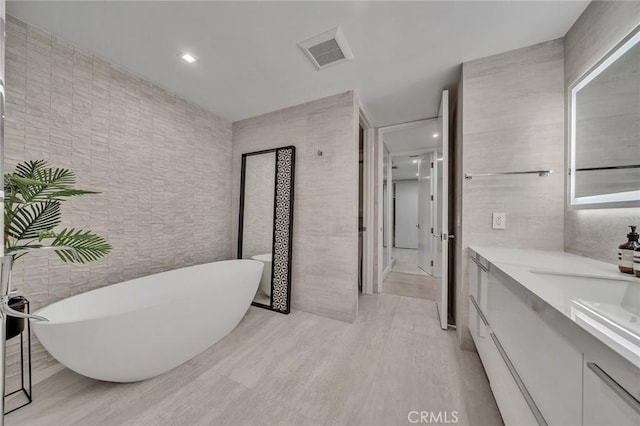 bathroom featuring a washtub, vanity, and tile walls