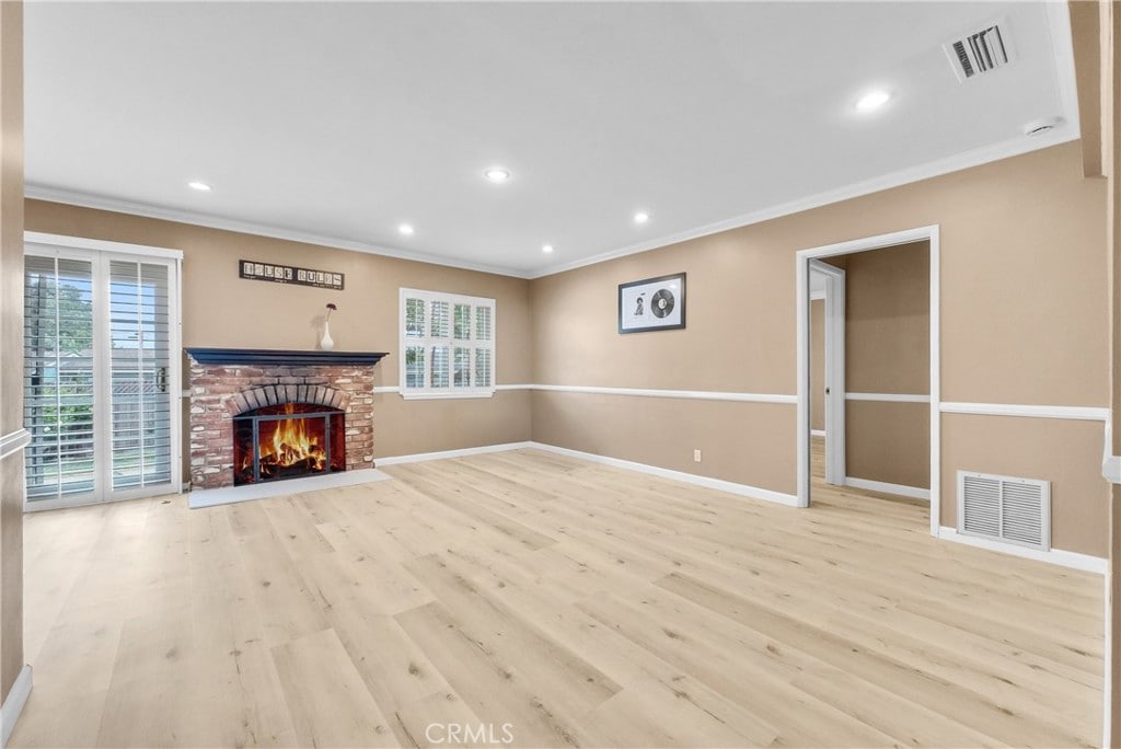 unfurnished living room featuring light wood-type flooring, ornamental molding, and a brick fireplace