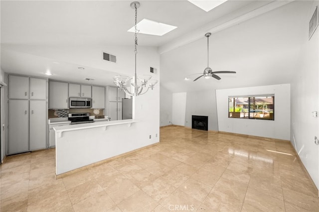 kitchen featuring a skylight, kitchen peninsula, stainless steel appliances, ceiling fan with notable chandelier, and decorative backsplash