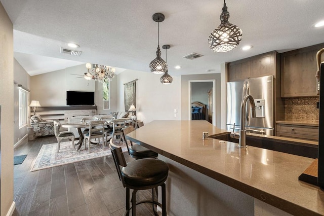 kitchen featuring stainless steel refrigerator with ice dispenser, a breakfast bar area, decorative light fixtures, vaulted ceiling, and dark hardwood / wood-style flooring