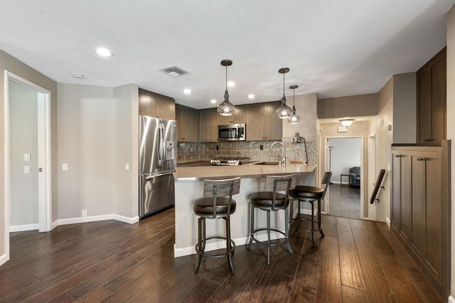 kitchen with sink, a breakfast bar area, appliances with stainless steel finishes, decorative light fixtures, and kitchen peninsula