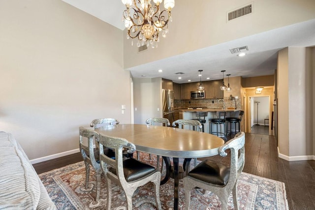 dining area with a towering ceiling, dark hardwood / wood-style floors, a chandelier, and sink