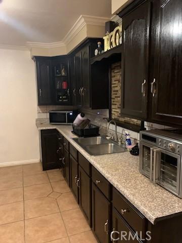 kitchen featuring crown molding, sink, light tile patterned floors, and dark brown cabinets