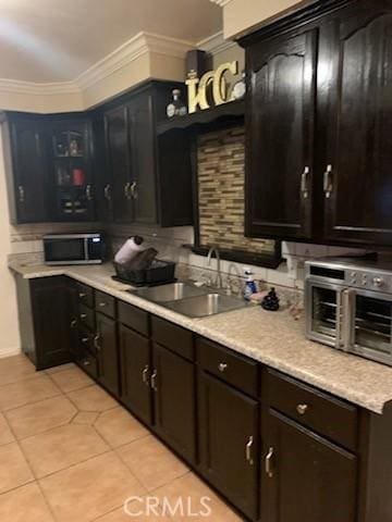 kitchen featuring dark brown cabinetry, crown molding, sink, and light tile patterned floors