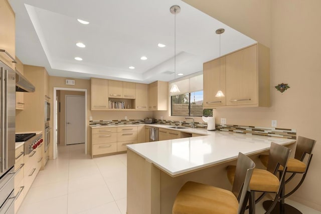 kitchen featuring light brown cabinets, hanging light fixtures, kitchen peninsula, a tray ceiling, and a breakfast bar area