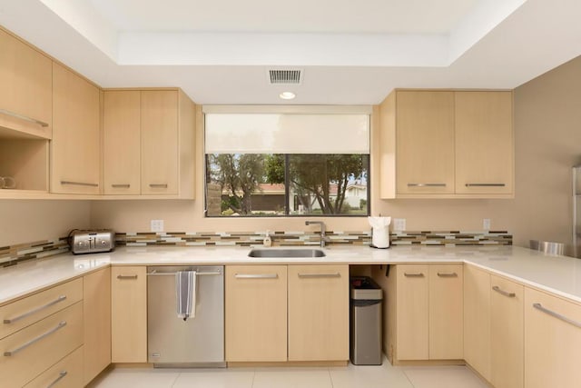 kitchen with light brown cabinetry, stainless steel dishwasher, a raised ceiling, and sink