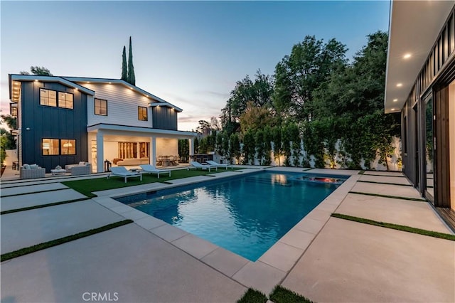 pool at dusk with a patio area and outdoor lounge area