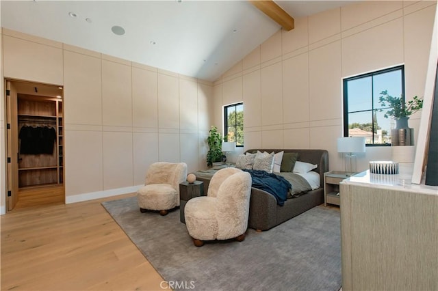 bedroom featuring a spacious closet, light hardwood / wood-style flooring, and lofted ceiling with beams