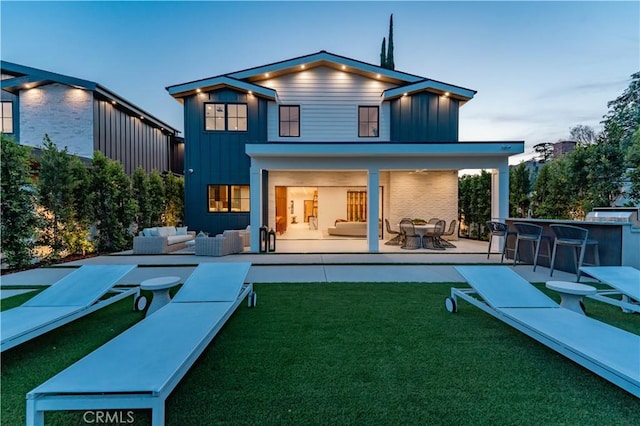 back house at dusk with a patio area, exterior bar, a yard, and an outdoor living space