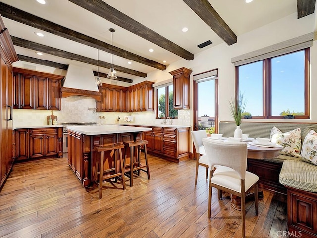 kitchen with premium range hood, light hardwood / wood-style floors, decorative light fixtures, a kitchen island, and beam ceiling