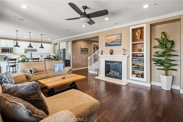 living room with ceiling fan, ornamental molding, built in features, and dark wood-type flooring