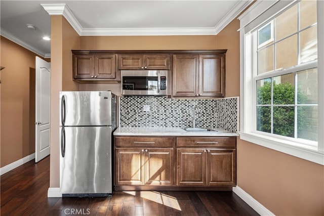 kitchen with appliances with stainless steel finishes, dark wood-type flooring, tasteful backsplash, crown molding, and sink