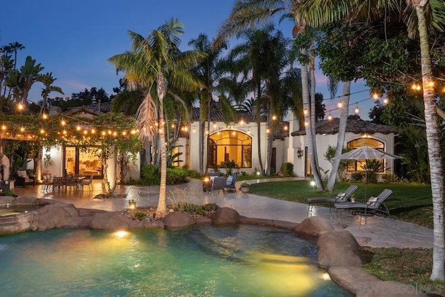 pool at dusk featuring a patio area and a lawn