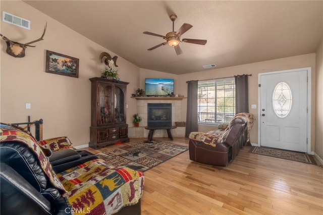 living room featuring ceiling fan, lofted ceiling, light hardwood / wood-style floors, and a tile fireplace