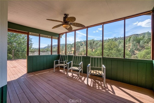 unfurnished sunroom featuring ceiling fan, a wealth of natural light, and a mountain view