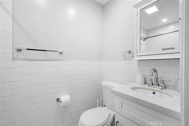 bathroom with vanity, toilet, and tile walls