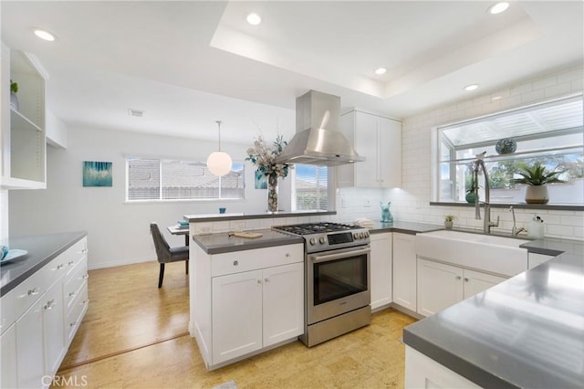 kitchen with high end range, ventilation hood, white cabinets, and a healthy amount of sunlight