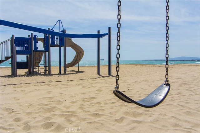 surrounding community featuring a playground, a water view, and a view of the beach