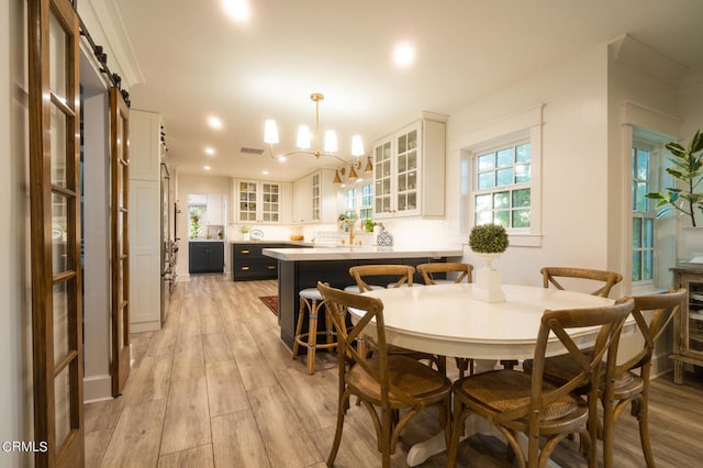 dining room featuring a barn door, light hardwood / wood-style floors, and an inviting chandelier