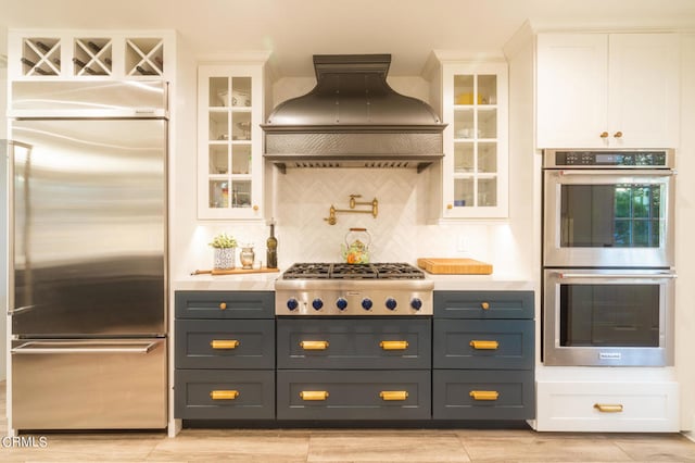 kitchen featuring stainless steel appliances, backsplash, custom range hood, and white cabinetry