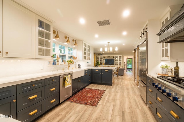 kitchen featuring light hardwood / wood-style floors, white cabinetry, hanging light fixtures, custom exhaust hood, and appliances with stainless steel finishes