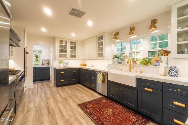 kitchen featuring light hardwood / wood-style floors, tasteful backsplash, white cabinets, dishwasher, and sink