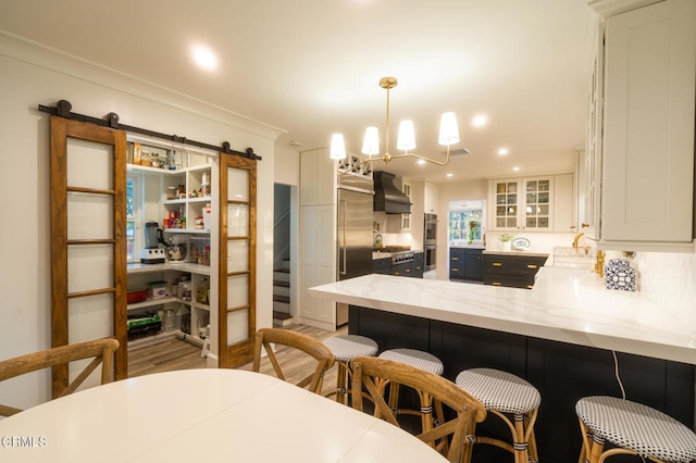 kitchen with hanging light fixtures, white cabinetry, a barn door, kitchen peninsula, and custom exhaust hood