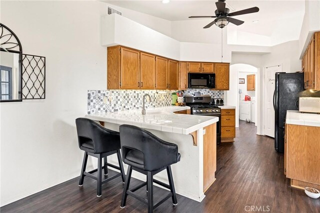 kitchen with backsplash, kitchen peninsula, dark hardwood / wood-style flooring, black appliances, and sink