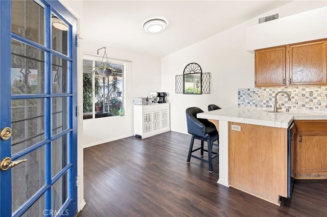 kitchen with kitchen peninsula, tasteful backsplash, dark wood-type flooring, a kitchen breakfast bar, and tile countertops