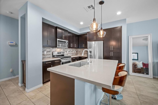 kitchen featuring dark brown cabinets, sink, a center island with sink, appliances with stainless steel finishes, and decorative light fixtures