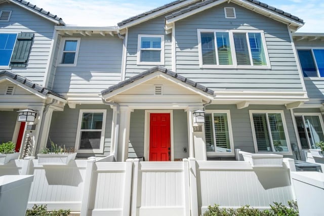 townhome / multi-family property featuring a fenced front yard, a tile roof, and a porch