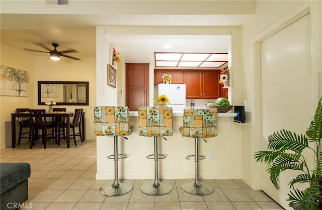 kitchen featuring kitchen peninsula, a breakfast bar, ceiling fan, light tile patterned floors, and white refrigerator