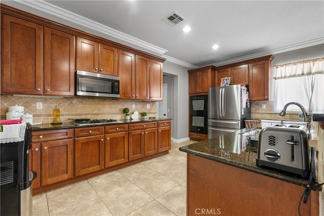 kitchen with light tile patterned flooring, ornamental molding, backsplash, appliances with stainless steel finishes, and dark stone counters