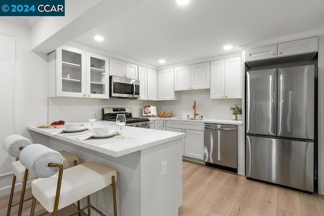 kitchen with a kitchen breakfast bar, sink, light hardwood / wood-style floors, white cabinetry, and stainless steel appliances