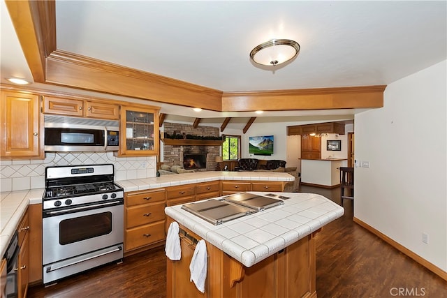 kitchen featuring appliances with stainless steel finishes, backsplash, dark hardwood / wood-style flooring, tile countertops, and a center island