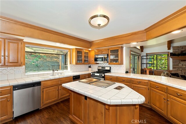 kitchen featuring appliances with stainless steel finishes, a center island, tile counters, dark hardwood / wood-style floors, and sink