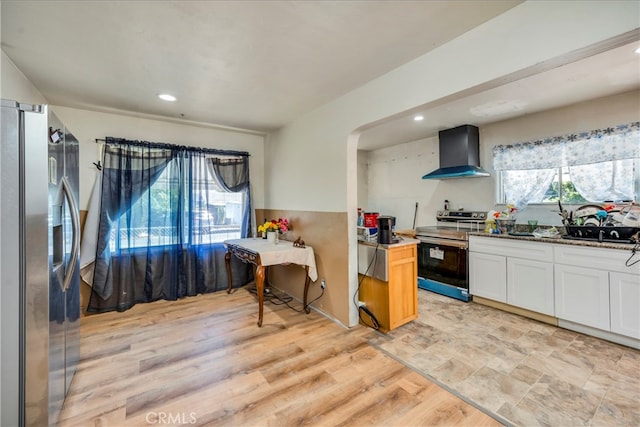 kitchen featuring wall chimney exhaust hood, stainless steel appliances, light hardwood / wood-style flooring, and plenty of natural light