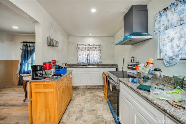 kitchen featuring white cabinets, wall chimney exhaust hood, stainless steel range with electric stovetop, a center island, and sink