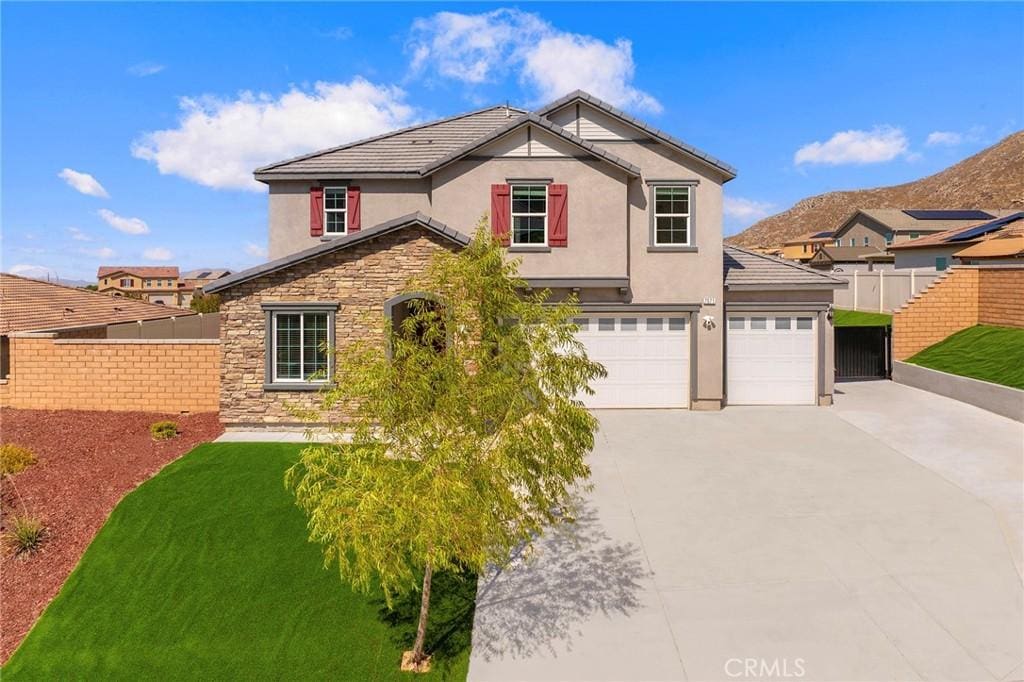 traditional-style house featuring a garage, concrete driveway, stone siding, fence, and stucco siding