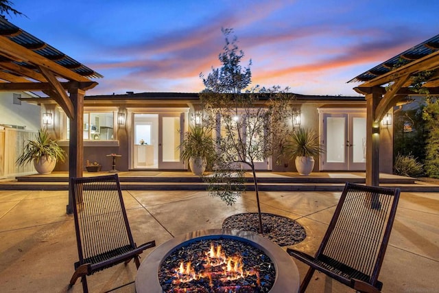 patio terrace at dusk featuring an outdoor fire pit and french doors