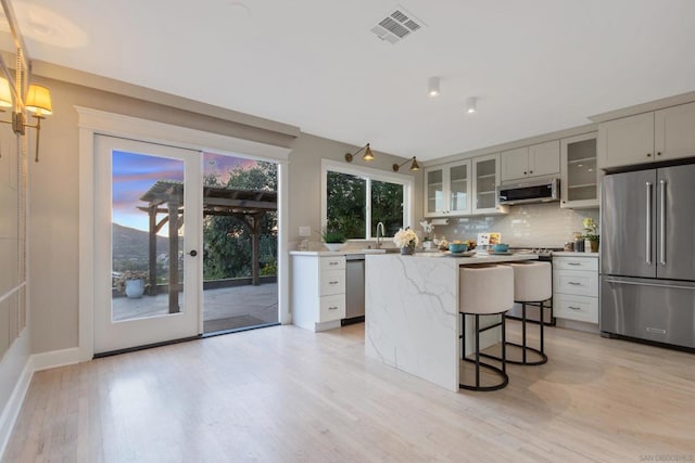 kitchen with decorative light fixtures, backsplash, light hardwood / wood-style flooring, appliances with stainless steel finishes, and a center island