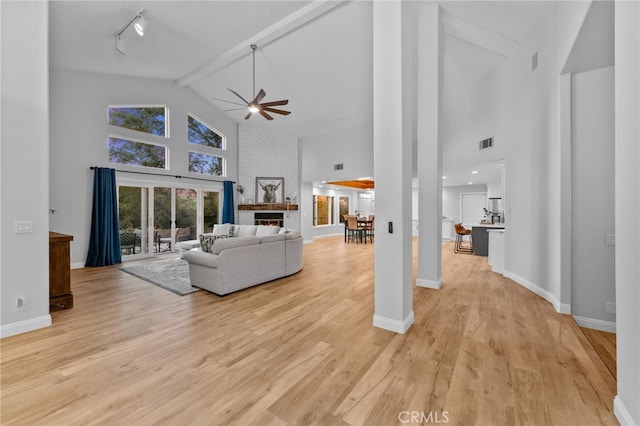 living room with beam ceiling, high vaulted ceiling, track lighting, light hardwood / wood-style floors, and a brick fireplace