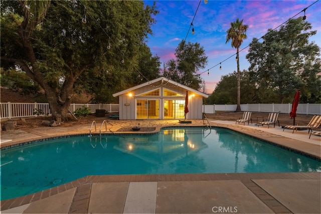 pool at dusk with a patio and an outbuilding