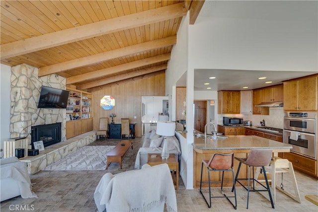 living room with a stone fireplace, sink, vaulted ceiling with beams, and wooden ceiling