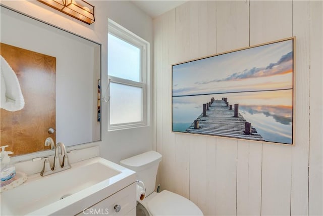 bathroom with vanity, toilet, and wood walls