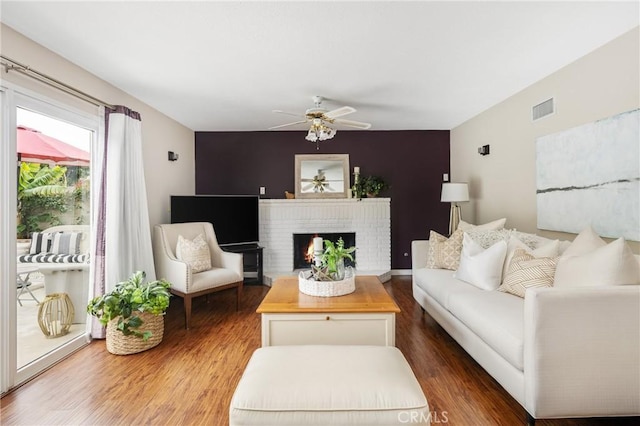 living room with a brick fireplace, dark hardwood / wood-style floors, and ceiling fan