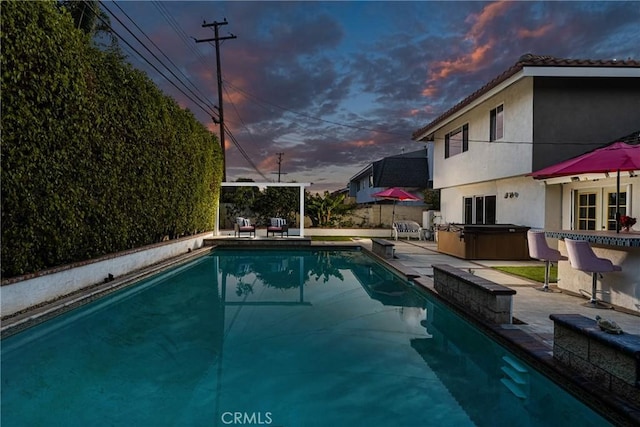 pool at dusk featuring a hot tub and a patio area